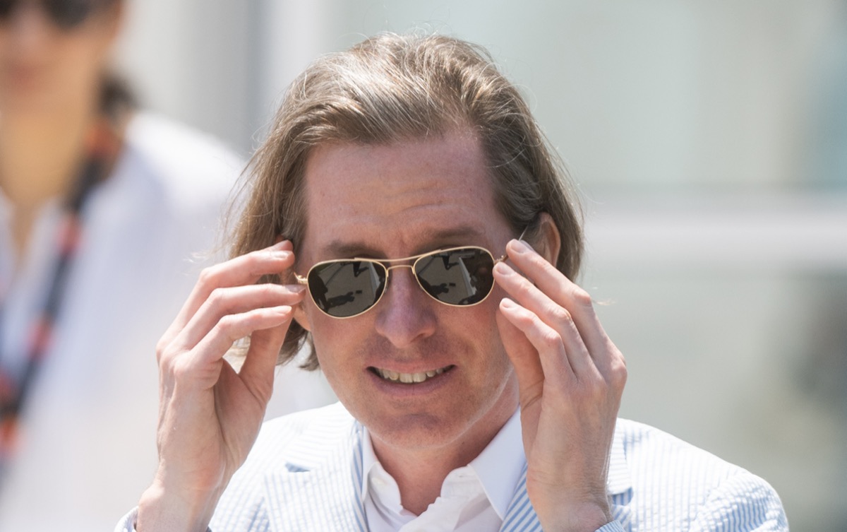 Wes Anderson adjusting his sunglasses.