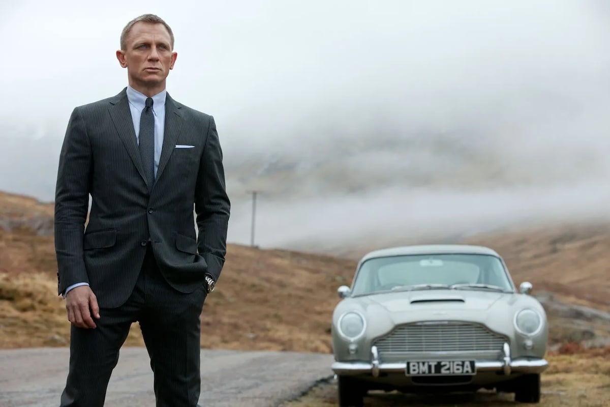The smartly dressed James Bond standing on a country road in front of a white luxury car in "Skyfall"