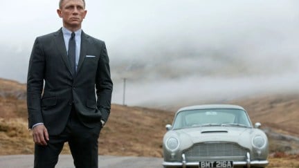 The smartly dressed James Bond standing on a country road in front of a white luxury car in 