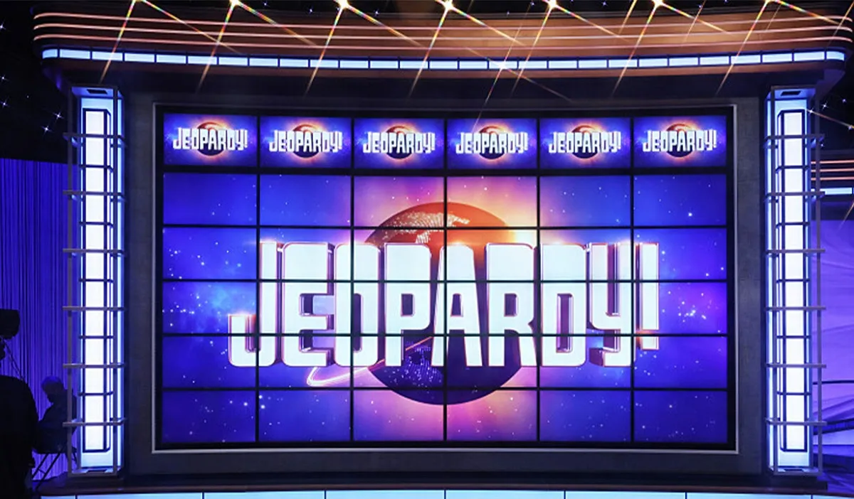 Image of the 6x6 grid of screens that make up the question board on the set of 'Jeopardy!' There are no questions or categories on the screens. The top six screens feature the 'Jeopardy!' logo in each one, and the rest of the screens each contain an image that add up to one larger 'Jeopardy!' logo.