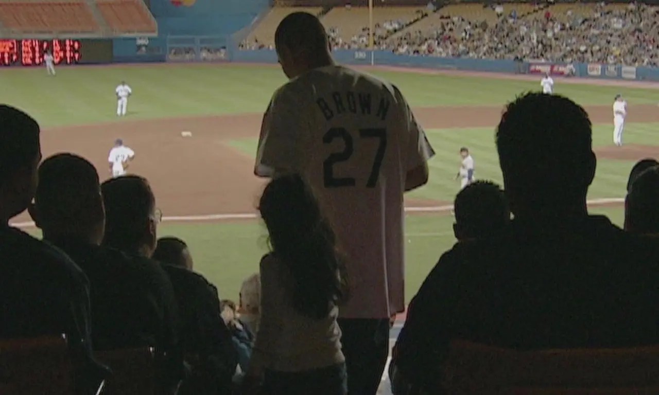 A man in a jersey walks through the stands at a baseball game with his young daughter in the documentary 'Long Shot'