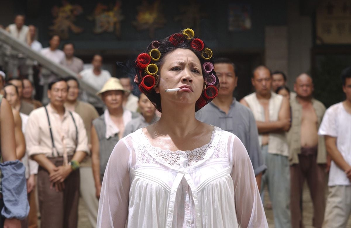 A woman in the film "Kung Fu Hustle" stands looking irritated with rollers in her hair and smoking a cigarette.