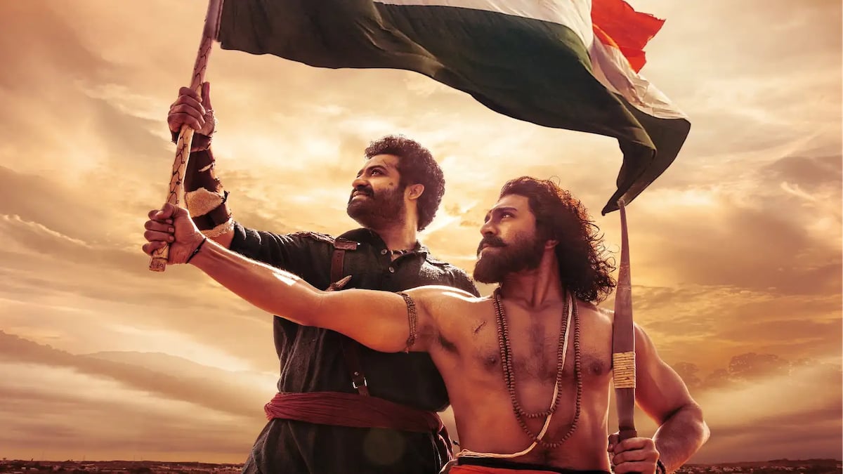The buff warriors Bheem and Ramaraju hold a flag while framed against a sunset sky in "RRR"