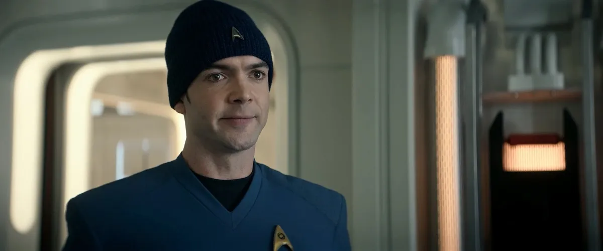Ethan Peck as Spock in a scene from 'Star Trek: Strange New Worlds.' We see Spock from the shoulders up. He's wearing his blue Starfleet uniform shirt with a black beanie with a Starfleet insignia on it over his ears. He's making a weird 