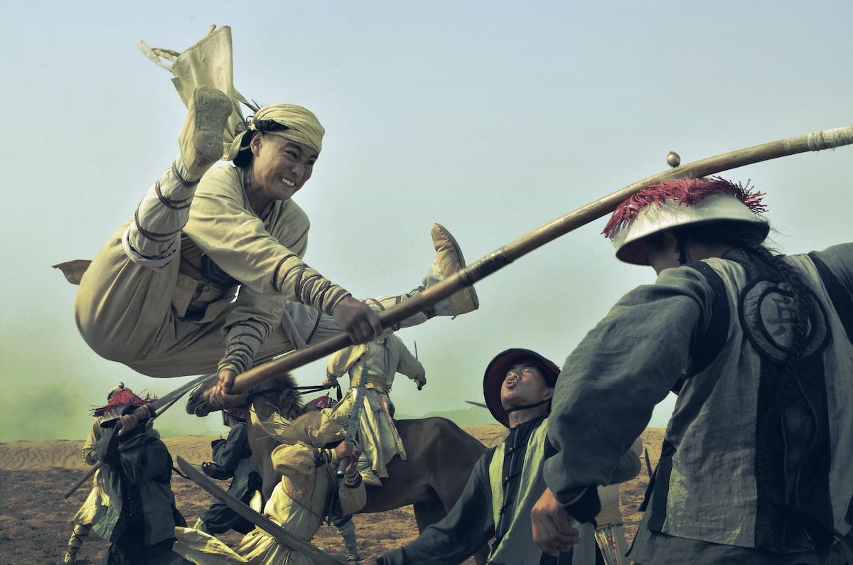 A martial arts practitioner in traditional Chinese attire, jumping over the heads of a group of assailants, hitting one of them on the head with a long piece of bamboo, from the film "Tai Chi Zero"