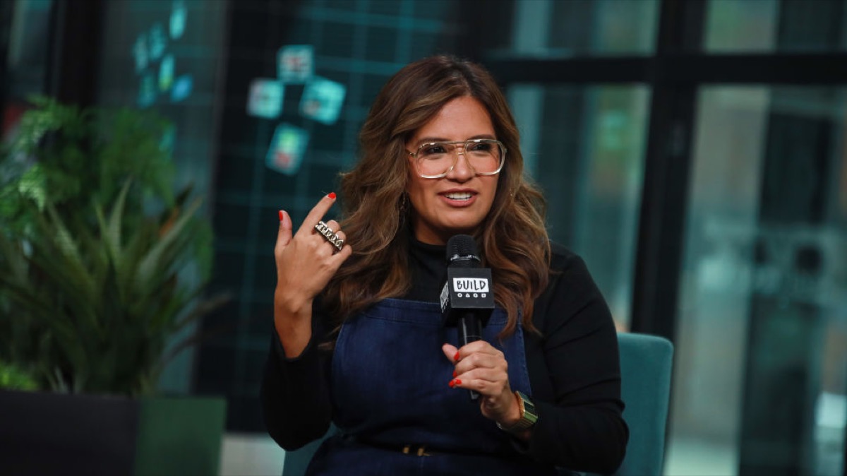 Cristela Alonzo holding a microphone, gesturing in confusion.