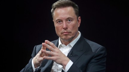 Elon Musk, alone against a black background, pressing his fingertips together and looking at the camera, displeased.