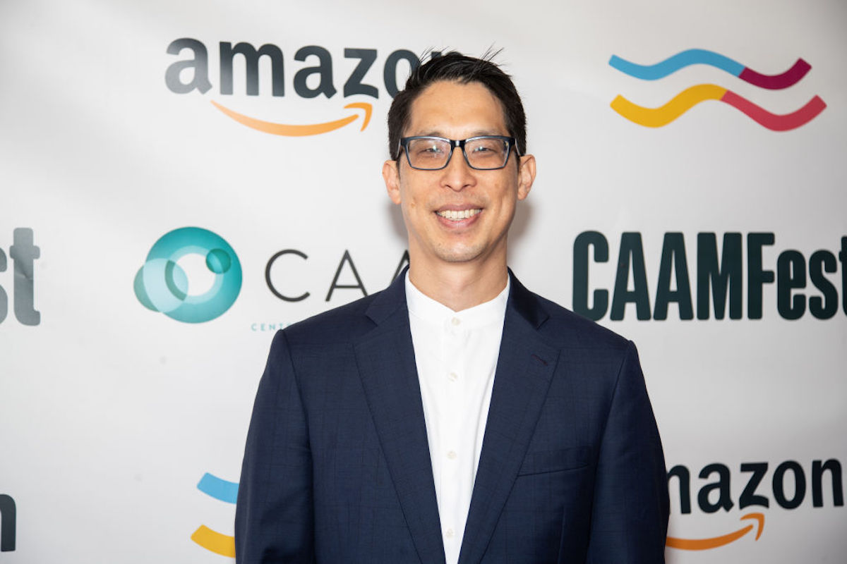 Gene Luen Yang smiles in front of a backdrop with corporate logos.