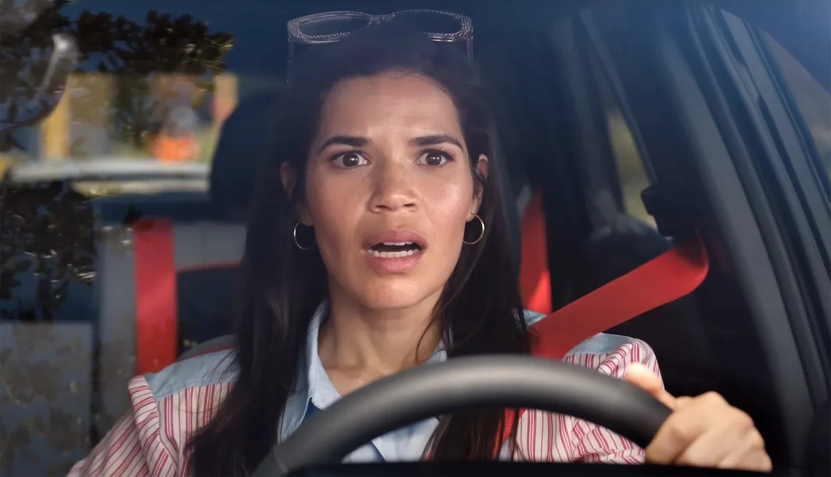 Gloria looks shocked, sitting behind the wheel of her car in Barbie.
