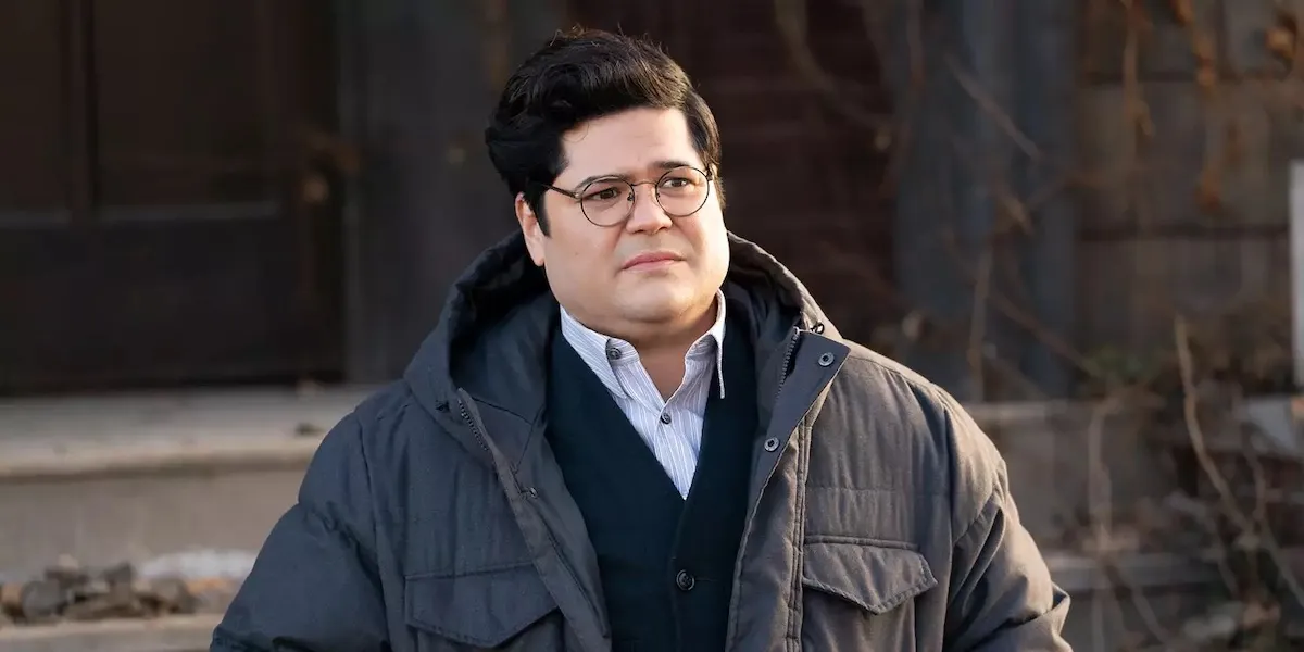 Guillermo purses his lips on the front steps of the vampires' house, wearing a winter jacket.