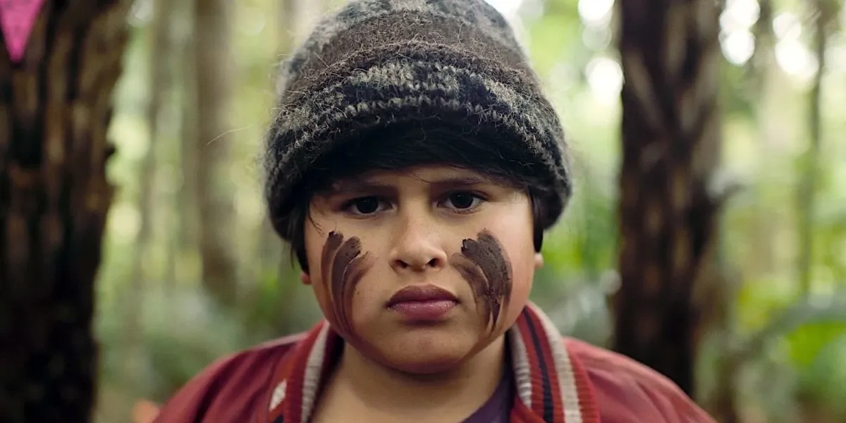 A young boy with faceprint on his cheeks frowns in the woods in "The Hunt For The Wilderpeople" 