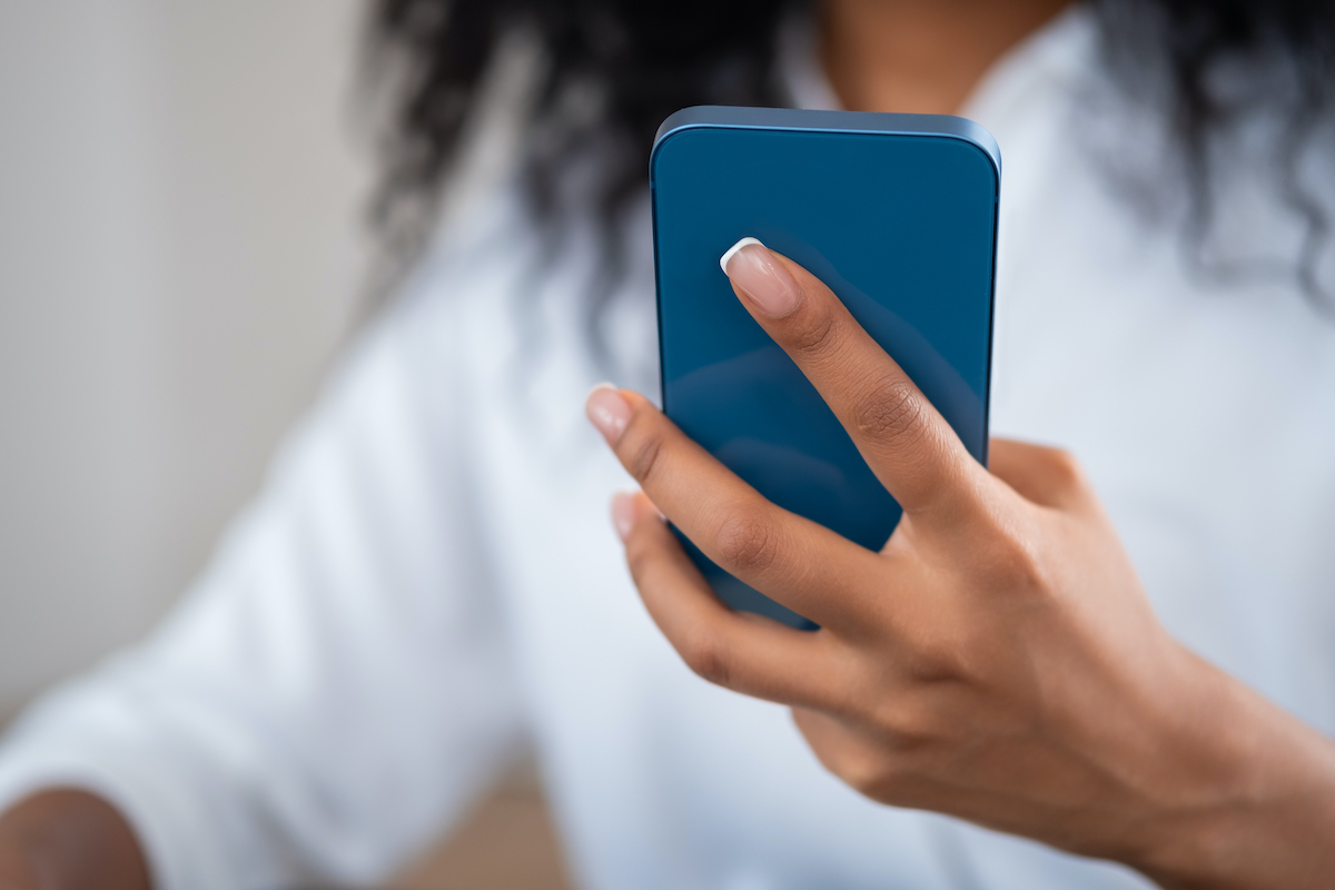 A woman with her face obscured holds her cell phone in front of her, looking at it.