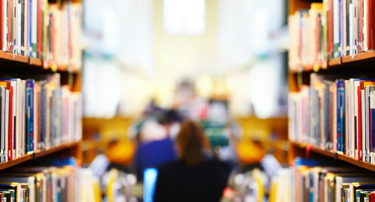A woman's figure is obscured sitting between library bookshelves.