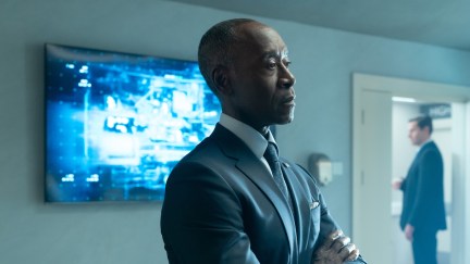 Rhodey folds his arms, looking unimpressed, with a TV screen behind him in Secret Invasion.