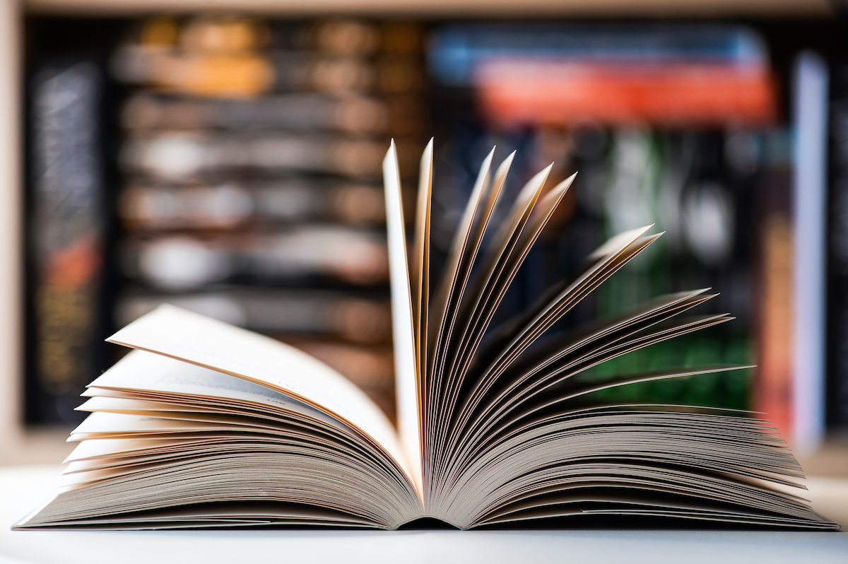 An open book on a table with book shelves in the background.