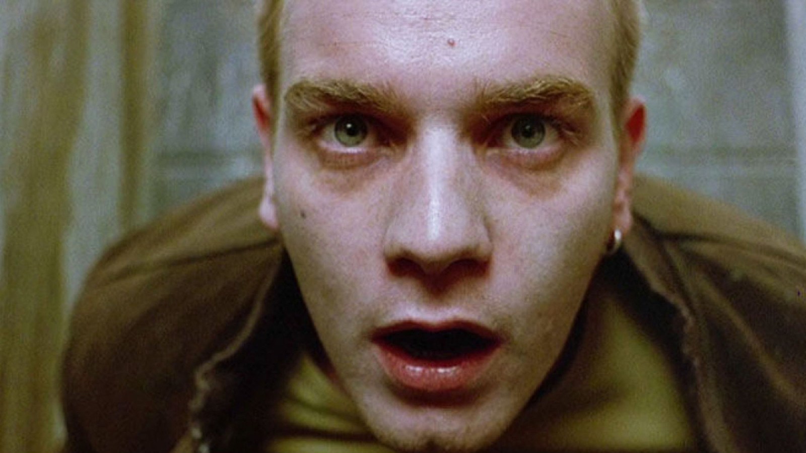 A close up of a white man looking upwards with red bags around his eyes in "Trainspotting"
