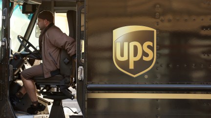 A UPS driver sits in the driver's seat of a UPS truck