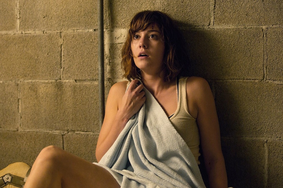 Mary Elizabeth Winstead as Michelle in a scene from Paramount's '10 Cloverfield Lane.' Ramona is a white woman with chin length brown hair and bangs. She's wearing a white undershirt and shorts and holding a white blanket up to her chest with a shocked expression on her face as she sits on the ground against a concrete basement wall.