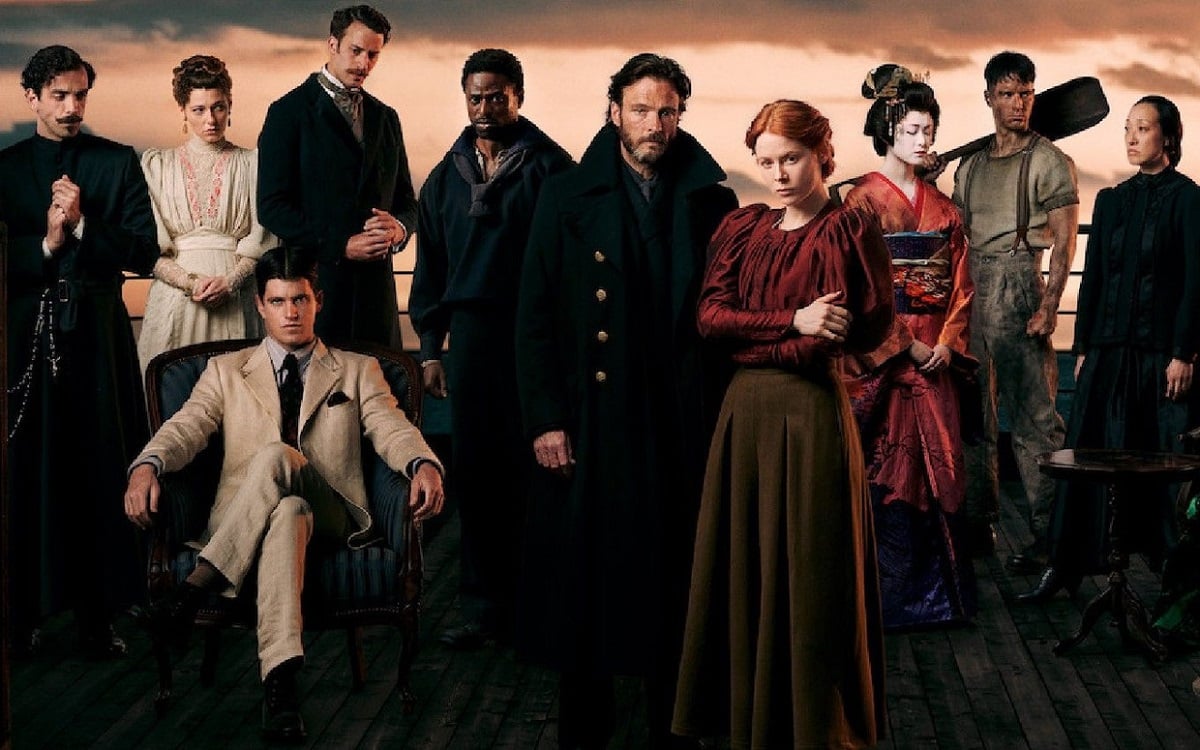 Promotional cast image for the Netflix show '1899.' It depicts 10 people on the deck of a ship dressed in 19th Century clothing. All are standing except for one man who sits cross-legged in an armchair on the left. Most are white except for one Black man and two Asian women.