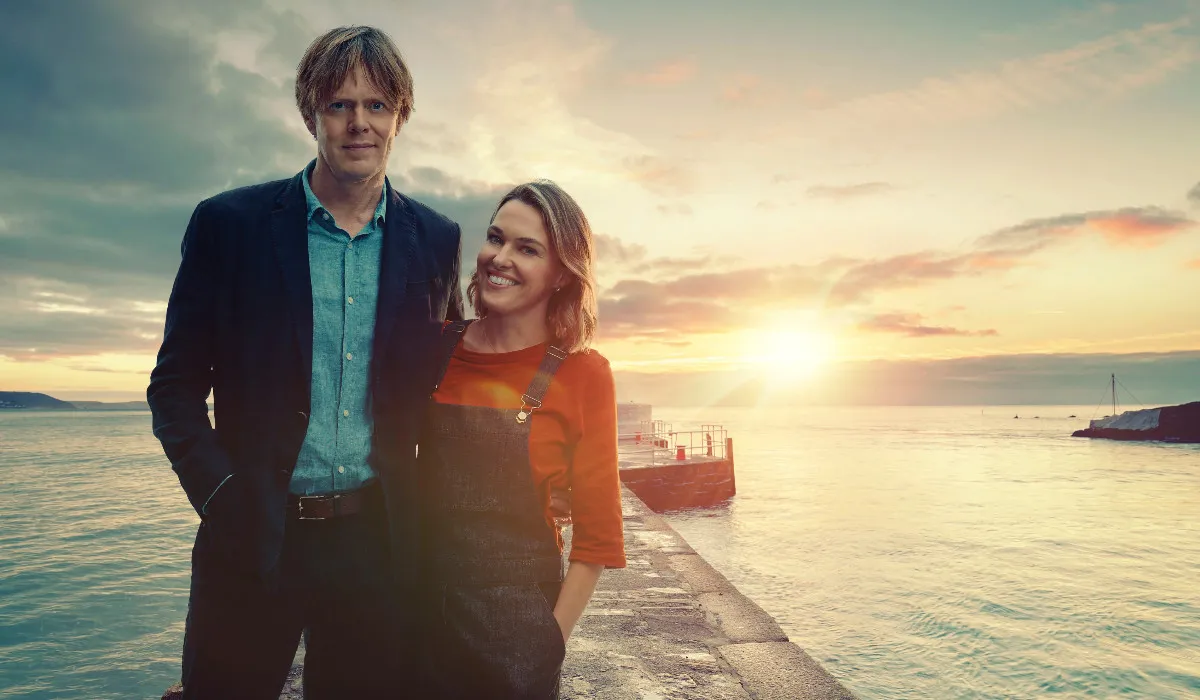 Kris Marshall as DI Humphrey Goodman and Sally Bretton as Martha Lloyd in Beyond Paradise, standing in front of a sunset