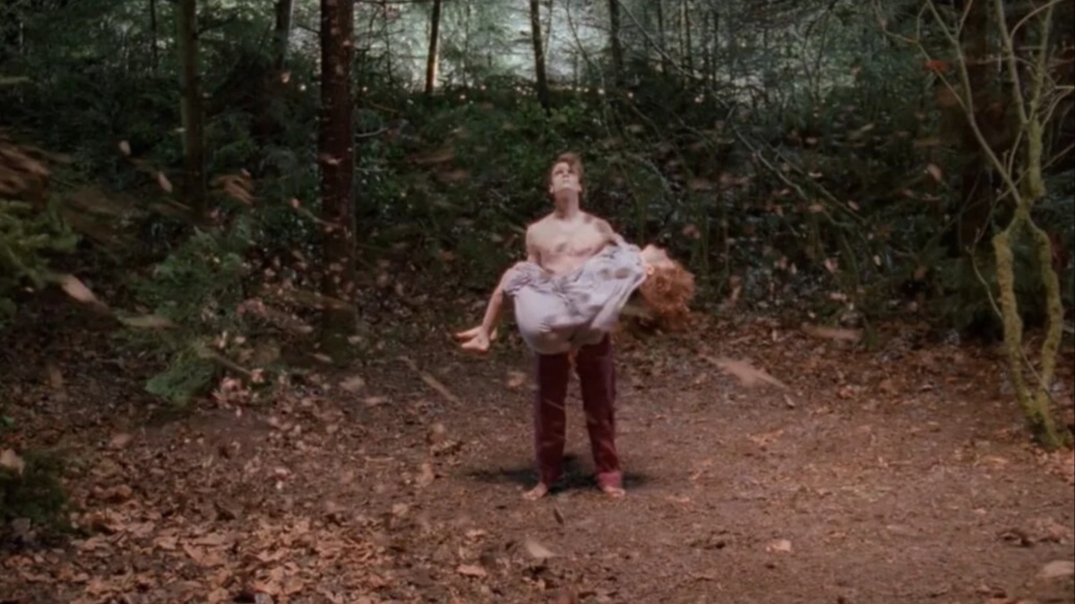 A person holding another person's seemingly lifeless body in the woods.
