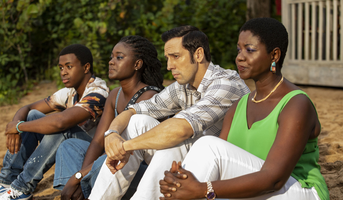 From left to right: Tahj Miles as Marlon Pryce, Shantol Jackson as Naomi Thomas, Ralf Little as Neville Parker, and Ginny Holder as Darlene Curtis in Death in Paradise's season 12 finale, sitting on the beach.