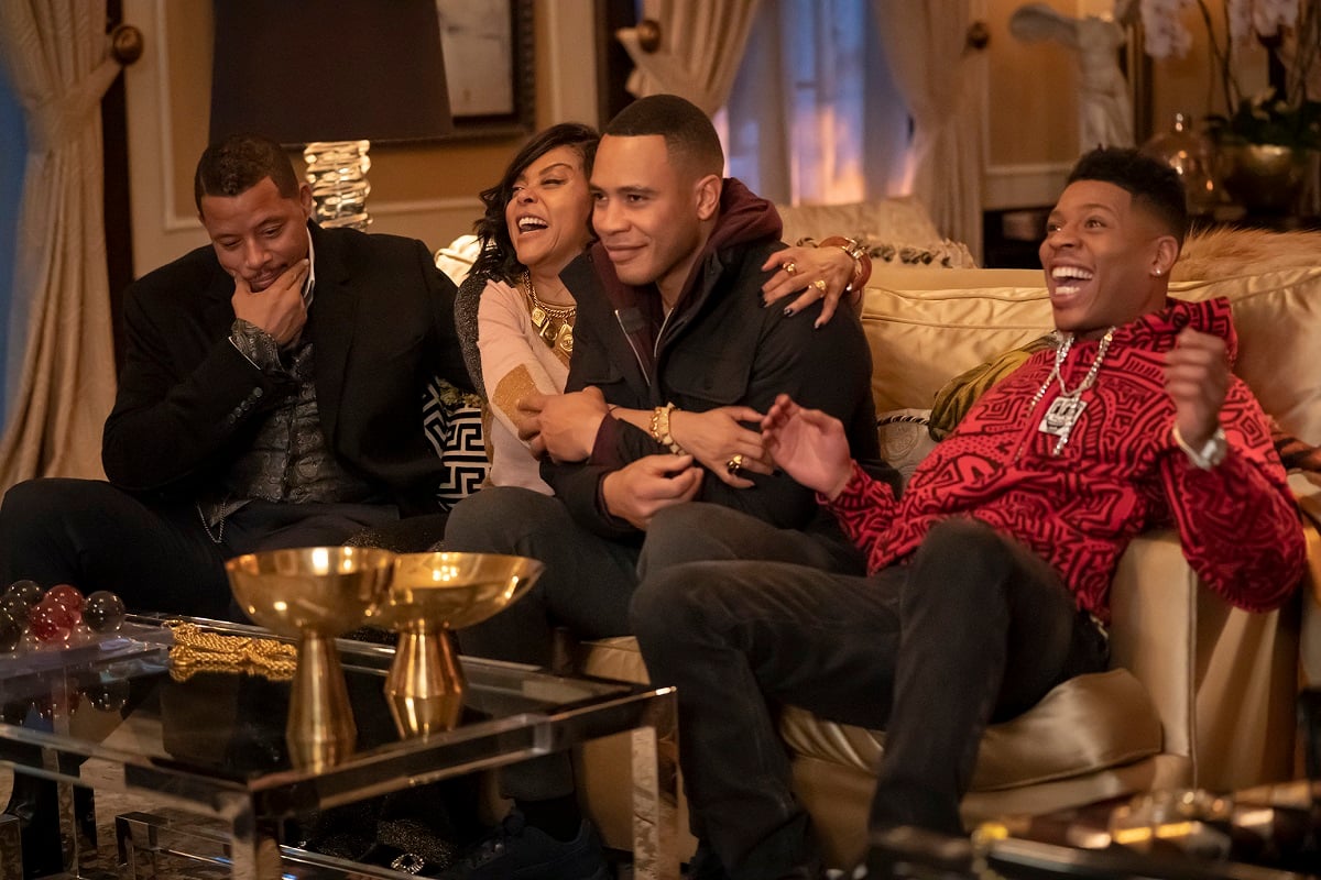 Terrence Howard, Taraji P. Henson, Trai Byers and Bryshere Y. Gray in a scene from the FOX show 'Empire.' They are a Black family sitting on a couch in a penthouse laughing. Howard sits on one end smirking and stroking his face thoughtfully. Henson has her arms around Byers as she laughs, and he's smiling as he holds her arms. Gray is on the other end with his smiling mouth open wide he sits back mid-clap cheering something. 