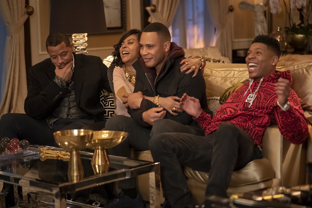 Terrence Howard, Taraji P. Henson, Trai Byers and Bryshere Y. Gray in a scene from the FOX show 'Empire.' They are a Black family sitting on a couch in a penthouse laughing. Howard sits on one end smirking and stroking his face thoughtfully. Henson has her arms around Byers as she laughs, and he's smiling as he holds her arms. Gray is on the other end with his smiling mouth open wide he sits back mid-clap cheering something.