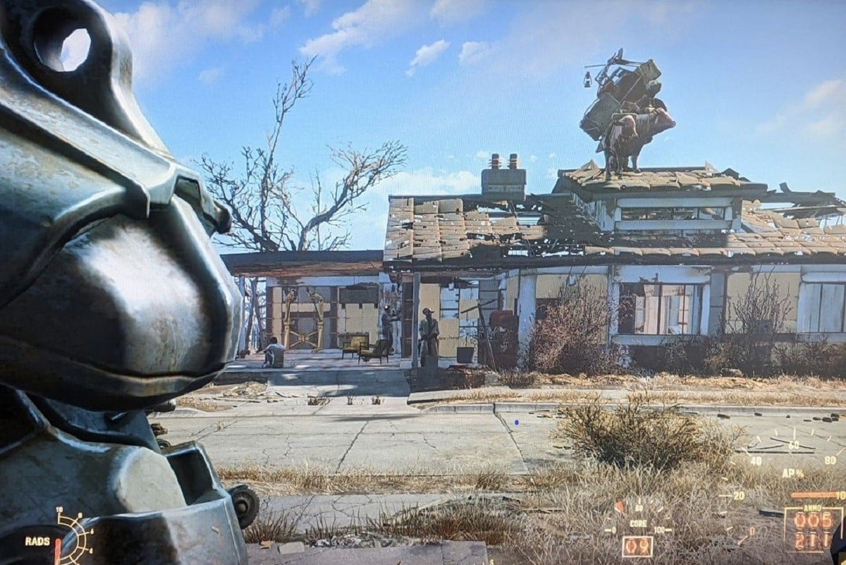 Screencap from the game 'Fallout 4.' Teresa Jusino's female player character is seen from behind wearing Power Armor while looking at a house where a pack Brahmin is standing on the roof.