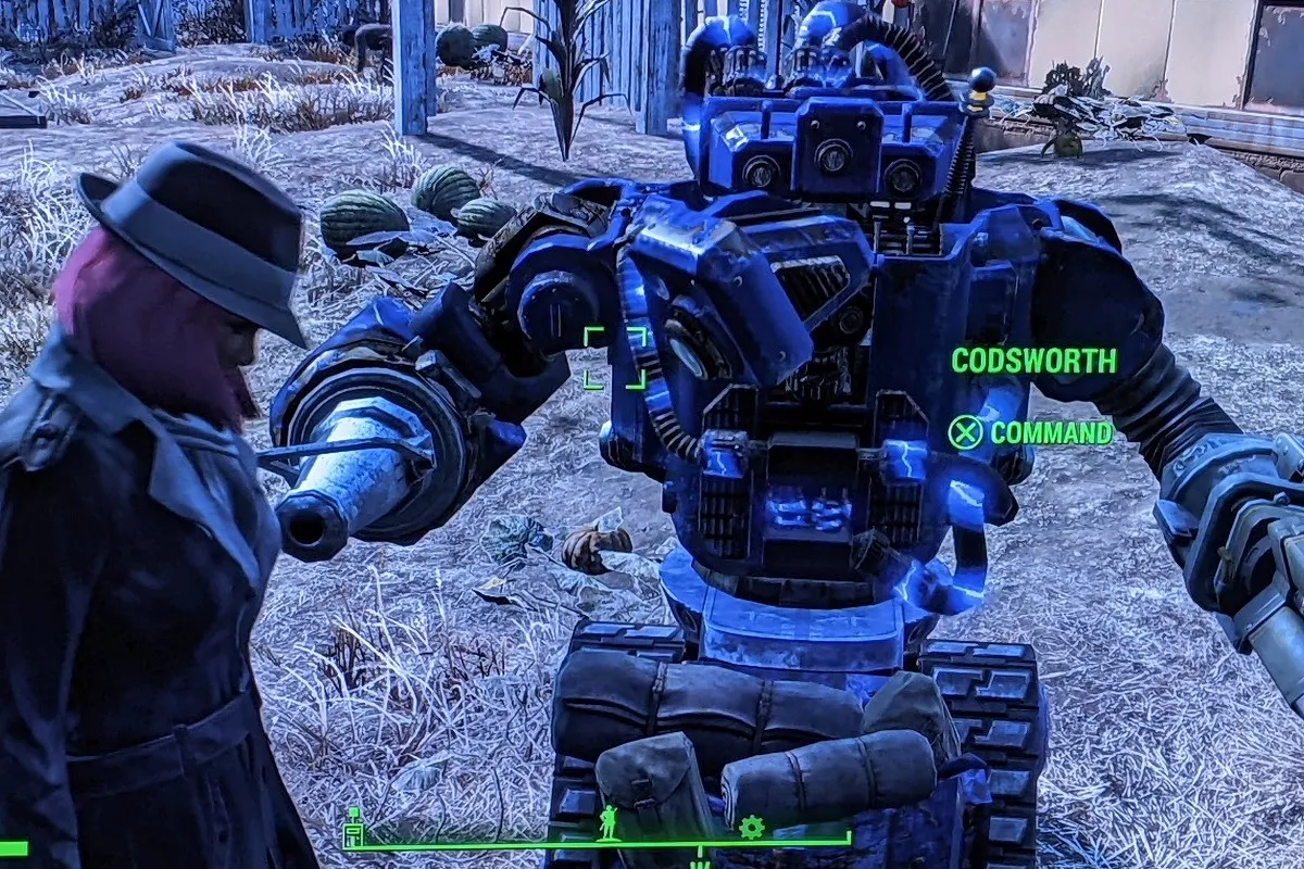 Screencap from the game 'Fallout 4.' Teresa Jusino's female player character wears the Silver Shroud trench coat and hat and has brown skin and a pink, chin-length bob. She's standing next to her robot companion, Codsworth, who is a tall, hefty blue robot on tank treads with a laser for one hand and a flamethrower for the other.
