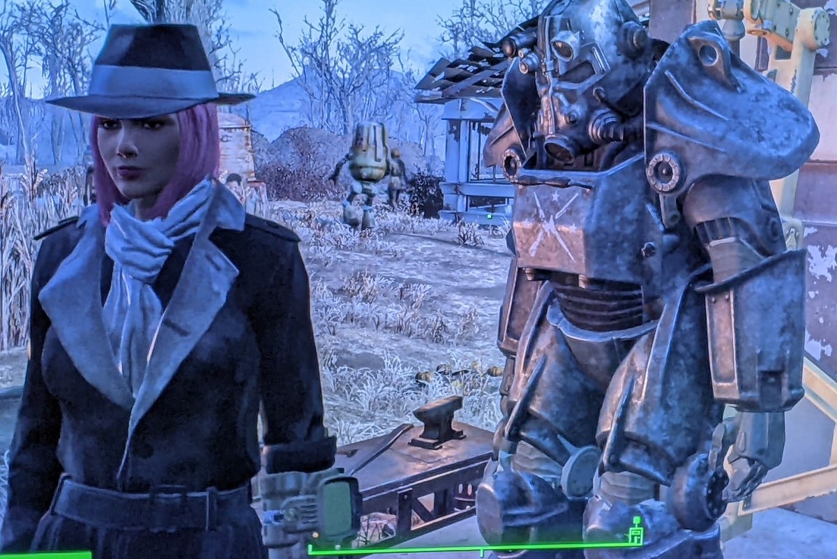 Screencap from the game 'Fallout 4.' Teresa Jusino's female player character is dressed in the Silver Shroud black trench coat and hat and has brown skin and a pink, chin-length bob. She's standing next to her Minuteman Power Armor at Sanctuary settlement.