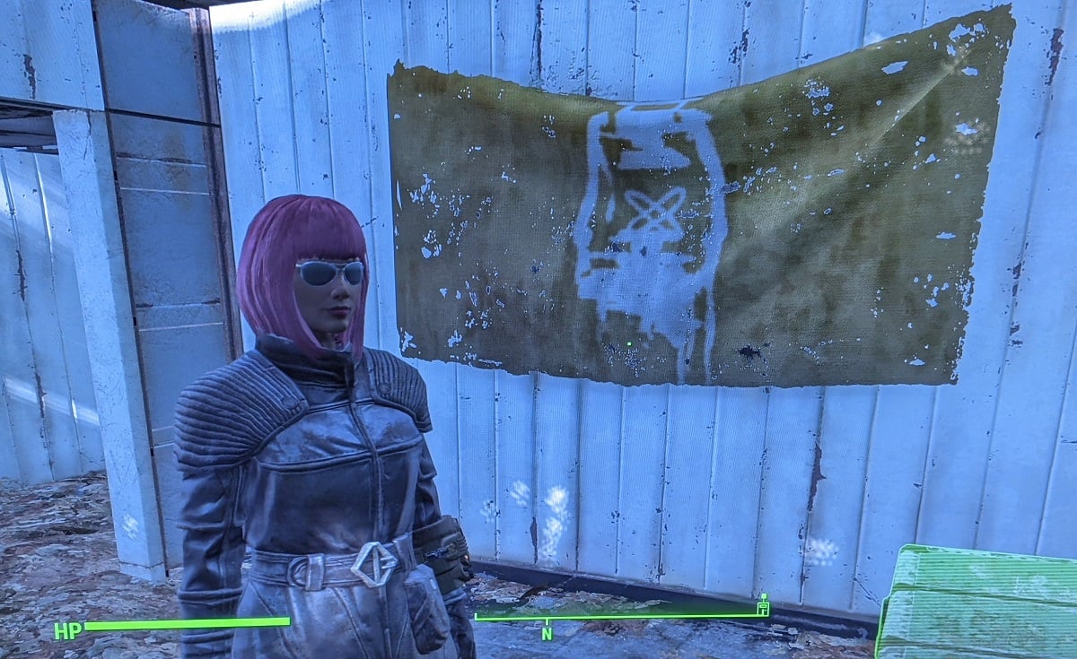 Screencap from the game 'Fallout 4.' Teresa Jusino's female player character wears the Institute Courser outfit and sunglasses, and has brown skin and a pink, chin-length bob. She's standing next to a Railroad flag hanging on her bedroom wall in Sanctuary.