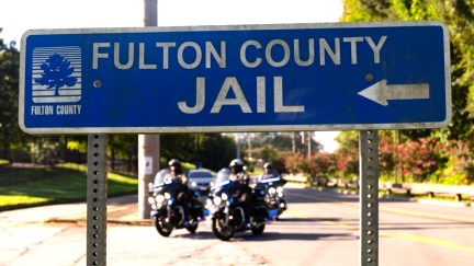 Road sign pointing to the Fulton County Jail, where Donald Trump and his co-conspirators are set to be booked in Atlanta, Georgia. Two police motorcycles are visible in the background.