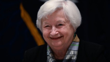 Janet Yellen from the shoulders up, against a black background, smiling.