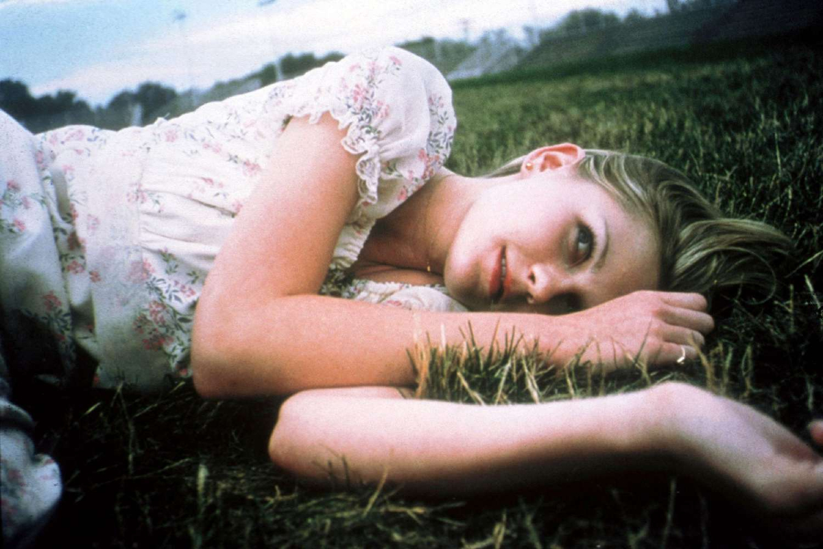 Lux Lisbon (Kirsten Dunst) lays in a grassy field and smiles wistfully in 'The Virgin Suicides'