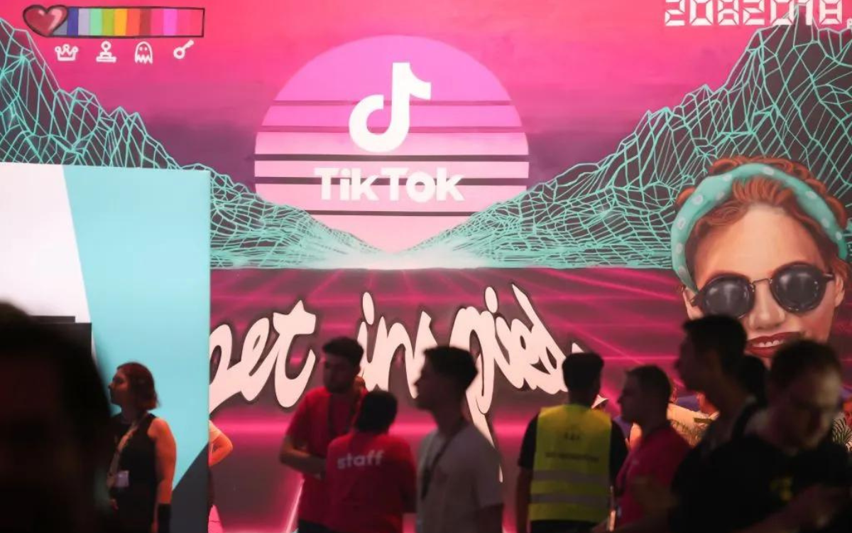 Gamers and Staff at a con standing in front a screen that has "Tiktok" in the center of it.