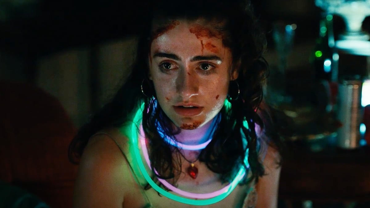 Rachel Sennott in 'Bodies Bodies Bodies': A young woman with blood on her face sits in the dark, illuminated by her glowing necklaces