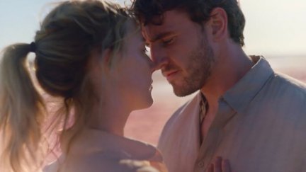 Image of Saoirse Ronan and Paul Mescal in a scene from the Amazon Studios film, 'Foe.' We see them standing outside from the shoulders up with their heads very close to each other as if they're about to kiss. They are both white. Ronan has blonde hair up in a ponytail and wears a white buttondown. Mescal has short, brown hair and a 5 o'clock shadow beard and wears a grey buttondown.