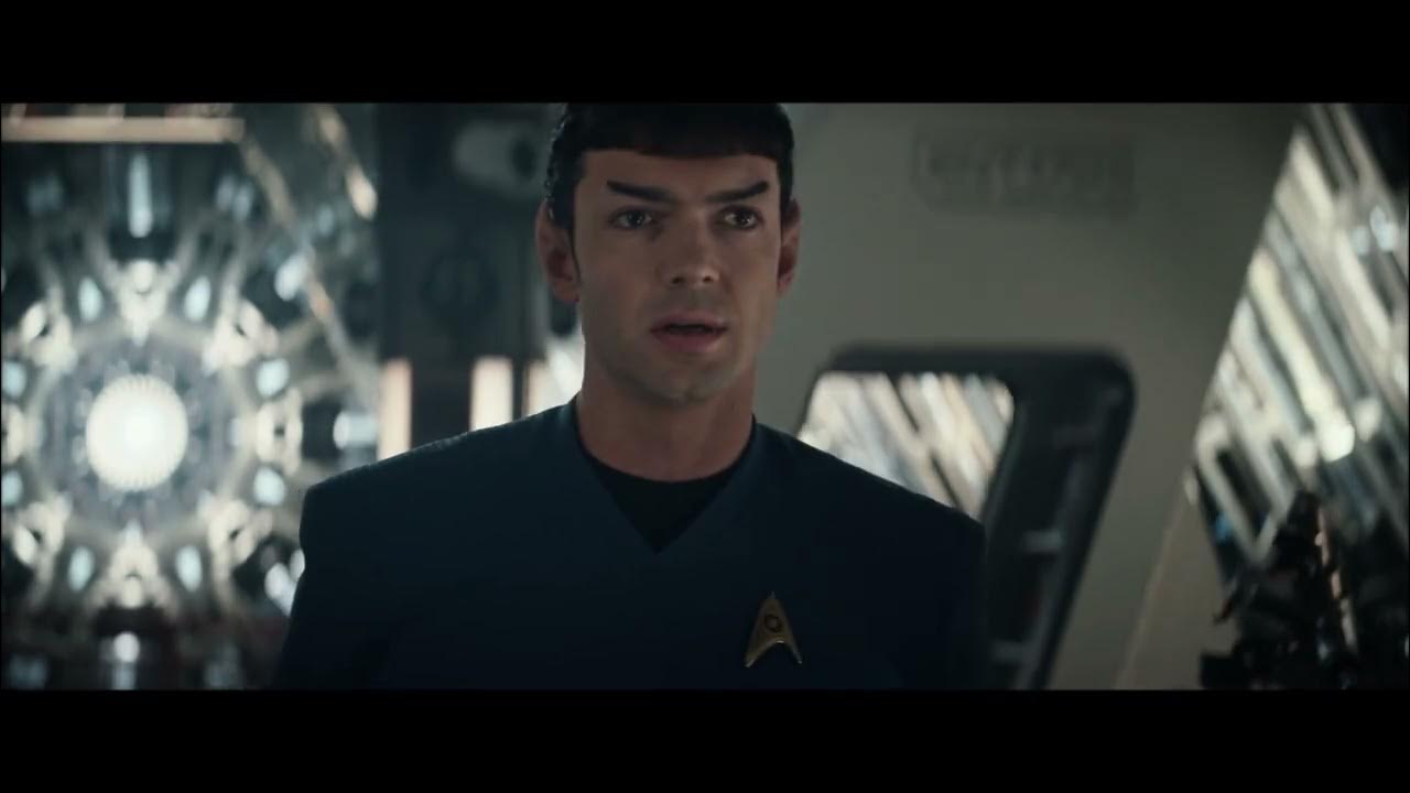 Image of Ethan Peck as Spock in a scene from 'Star Trek: Strange New Worlds.' He is a white Vulcan with pointed ears and short, black hair. He's wearing a blue Starfleet uniform and is looking off into the distance, despondent.