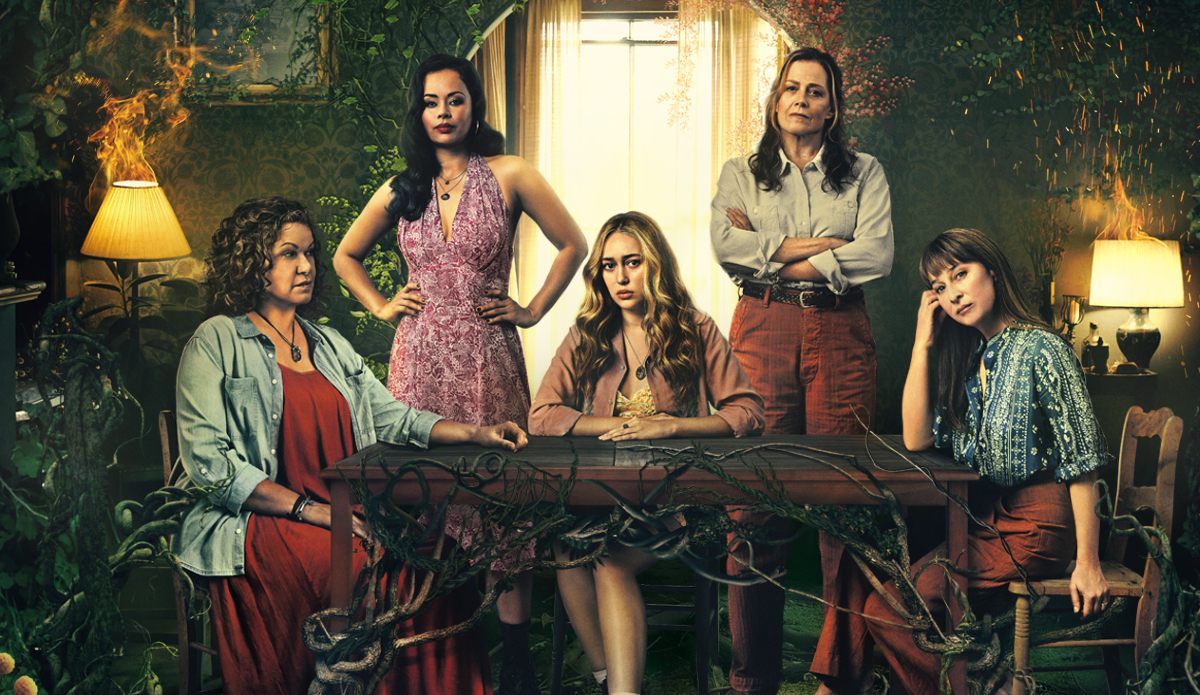 Five women sit around a table looking toward the camera while vines cover furniture and lamps in the background catch fire in 'The Lost Flowers of Alice Hart.'