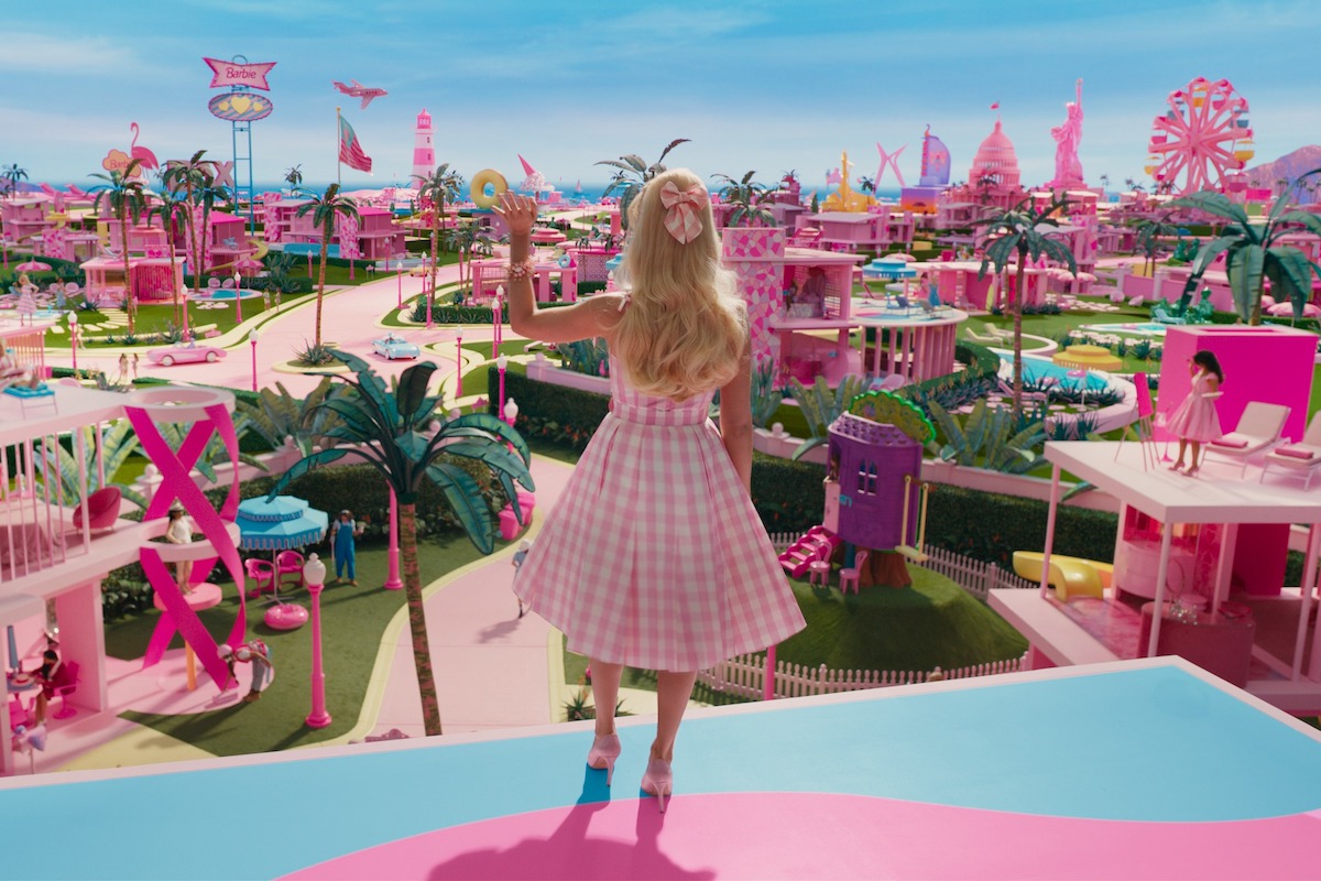 In a scene from Barbie, Barbie is seen from behind, waving to Barbieland from her balcony.