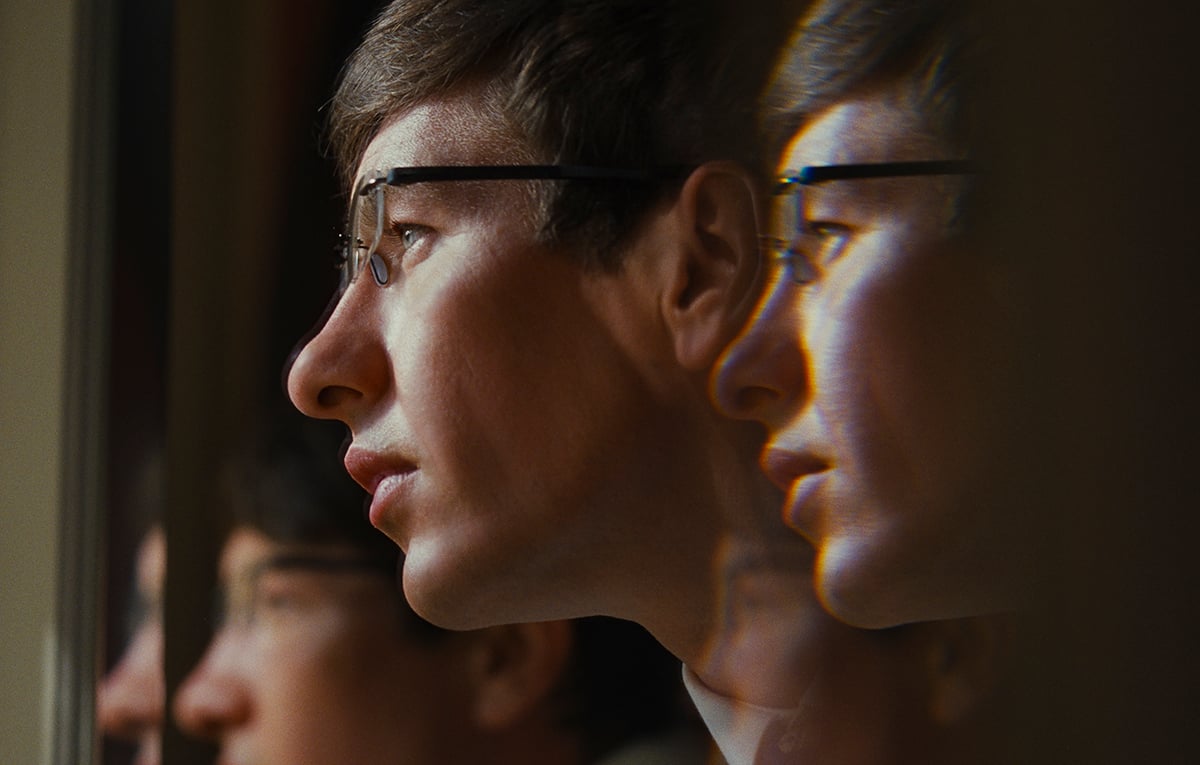 A white man with glasses has his reflection mirrored three times in "Saltburn"