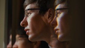 A white man with glasses has his reflection mirrored three times in 