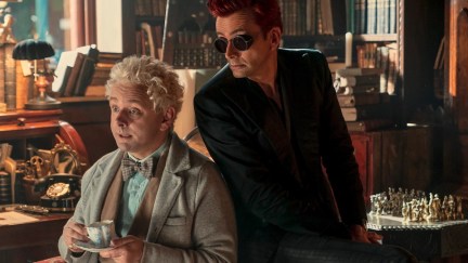 In 'Good Omens' season 2, Aziraphale (Michael Sheen) holds a cup of tea while Crowley (David Tennant) sits behind, wearing sunglasses. They are in Aziraphale's bookshop.
