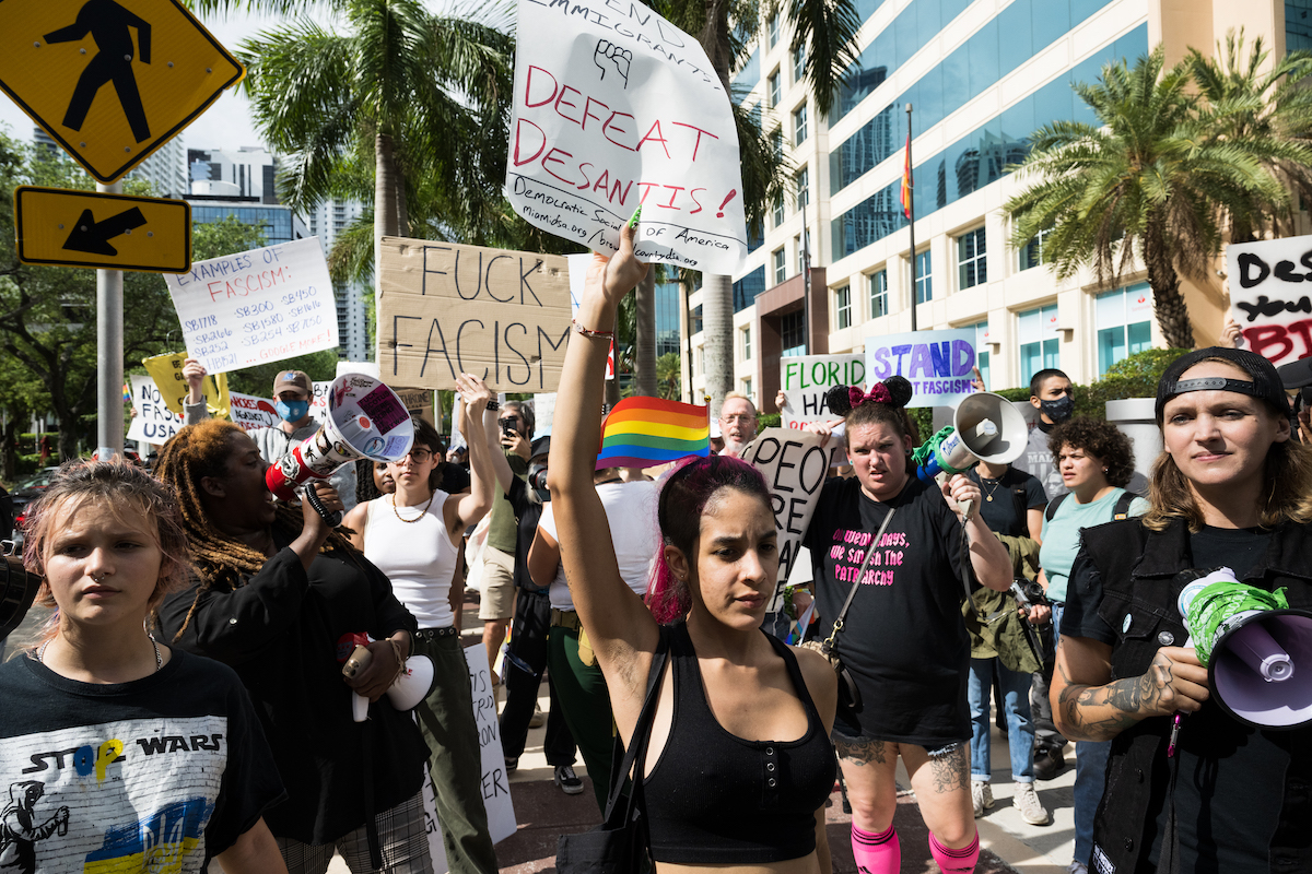 A crowd of protesters hold anti-Ron DeSantis, anti-fascism signs