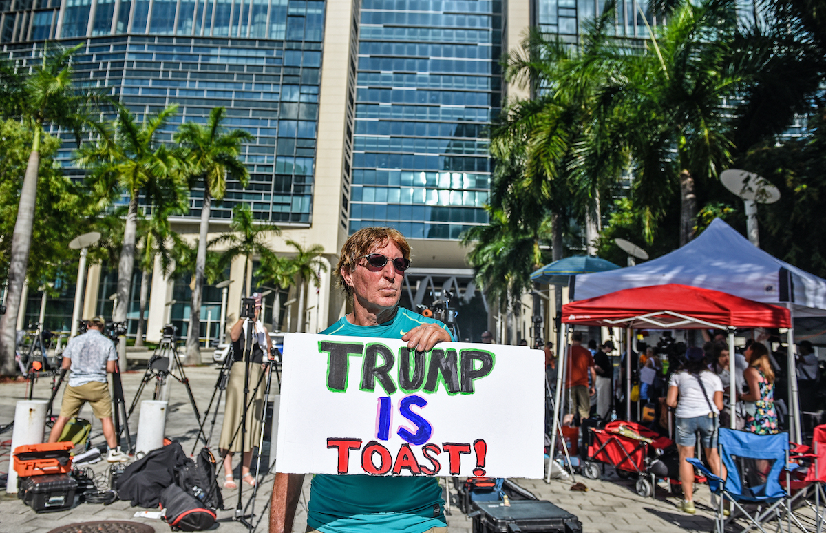A protester stands outside with a sign reading 'Trump is toast!'