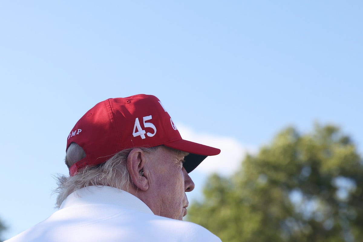Donald Trump, seen from behind from the shoulder up, wearing a red baseball cap bearing the number 45.