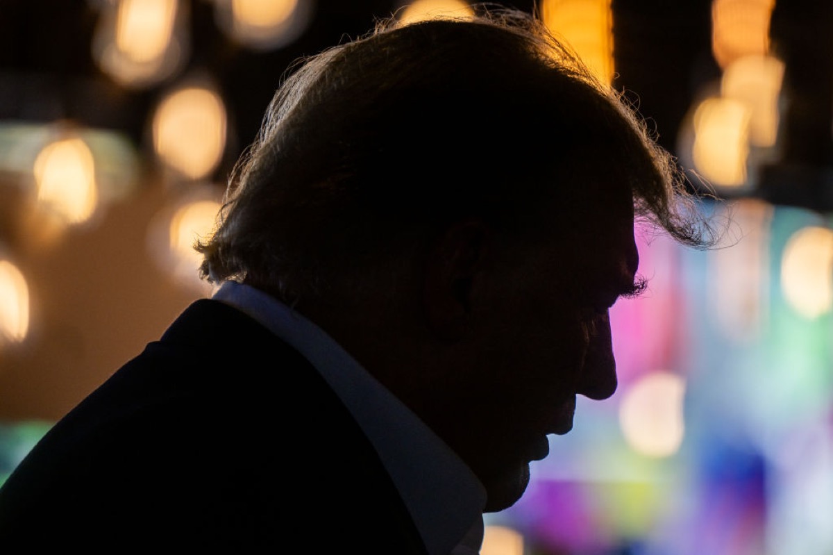 Donald Trump in profile, a dark silhouette against bright nighttime Iowa state fair lights.
