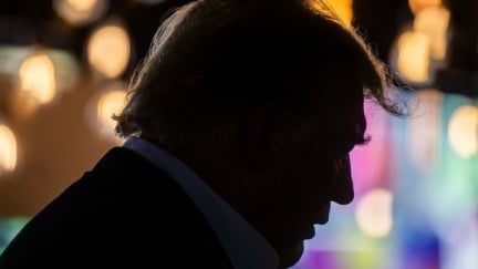Donald Trump in profile, a dark silhouette against bright nighttime Iowa state fair lights.