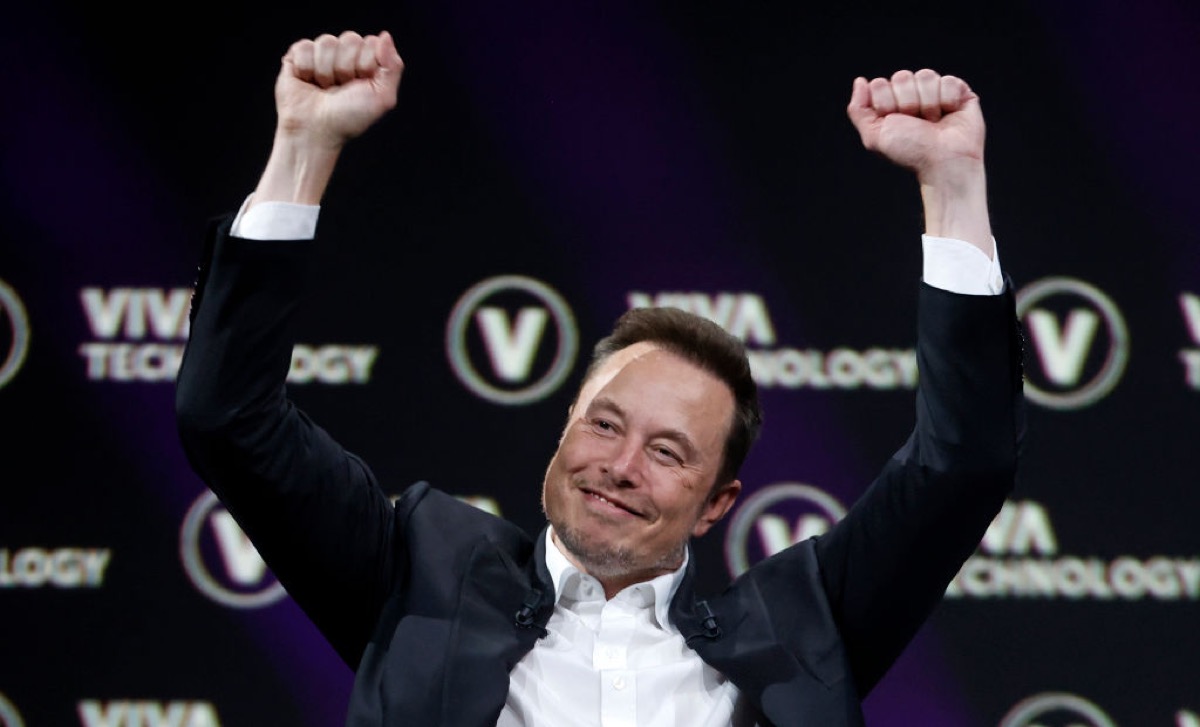 Elon Musk raises his arms triumphantly.